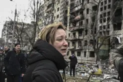 A woman reacts as she stands outside a ruined apartment